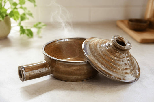 Brown ceramic microwave cooker with the lid off and steam rising in a bright kitchen.
