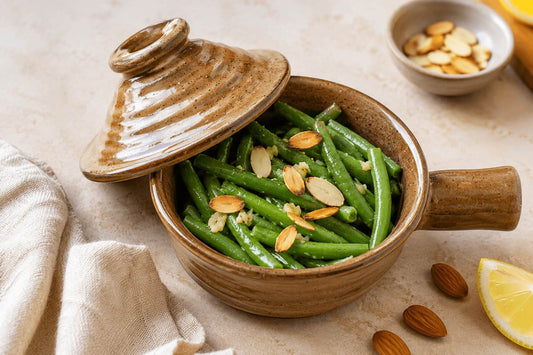 Green beans almondine in a ceramic microwave cooker with sliced almonds and lemon.