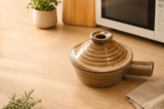 Brown ceramic microwave cooker with lid on a wooden countertop near a microwave.