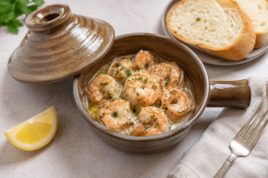 Shrimp scampi in a ceramic microwave cooker with lemon wedges nearby.
